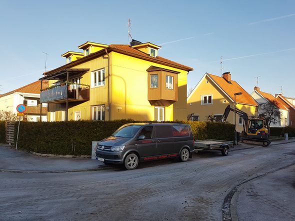 Gult hus där solen lyser på fasaden, bil i förgrunden